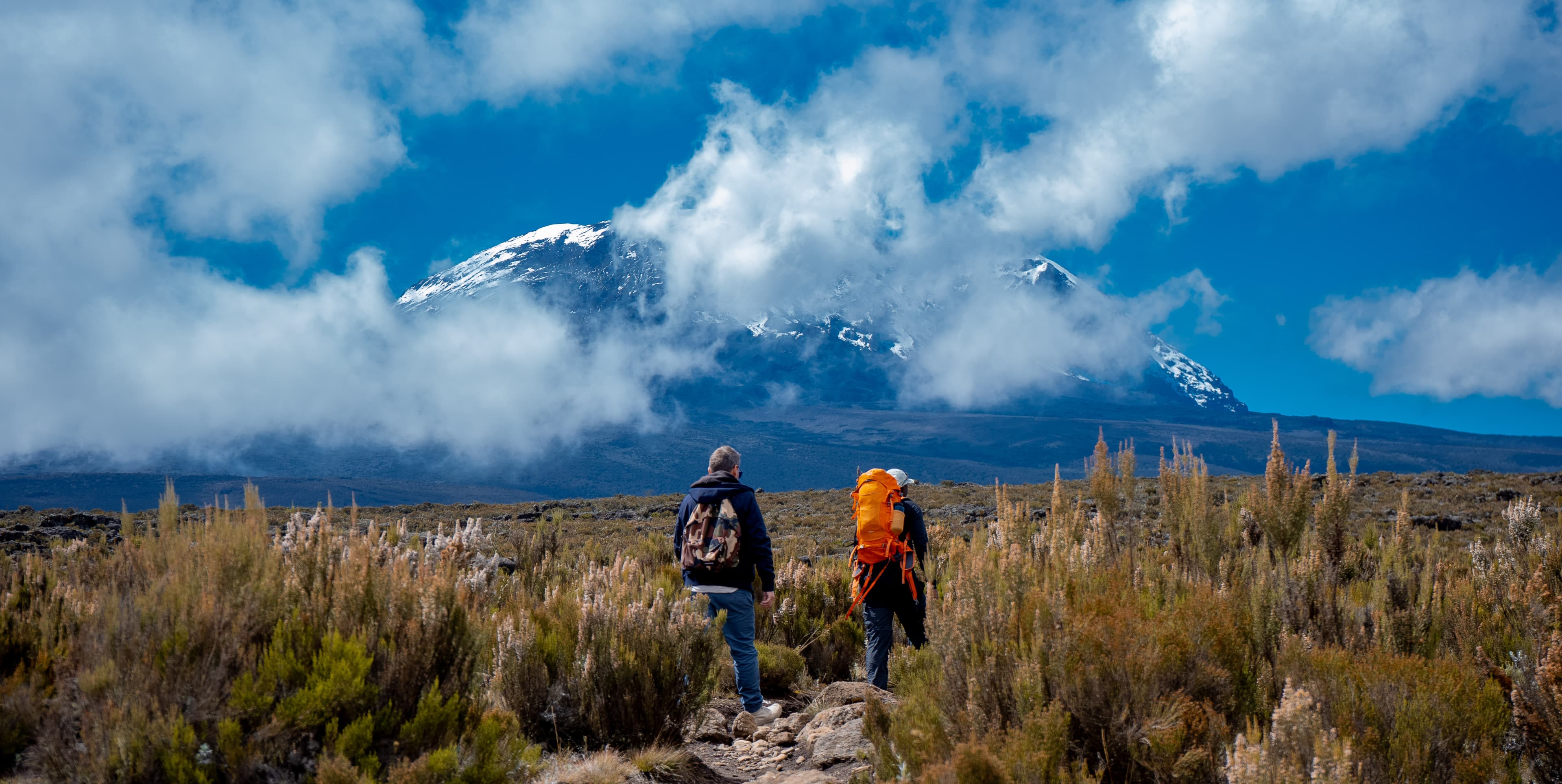 Climbers approaching Kilimanjaro beneath drifting clouds